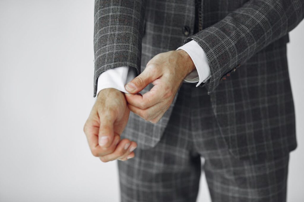 pexels photo 4975613 Close-up of a man adjusting his plaid suit, showcasing elegant formal wear.